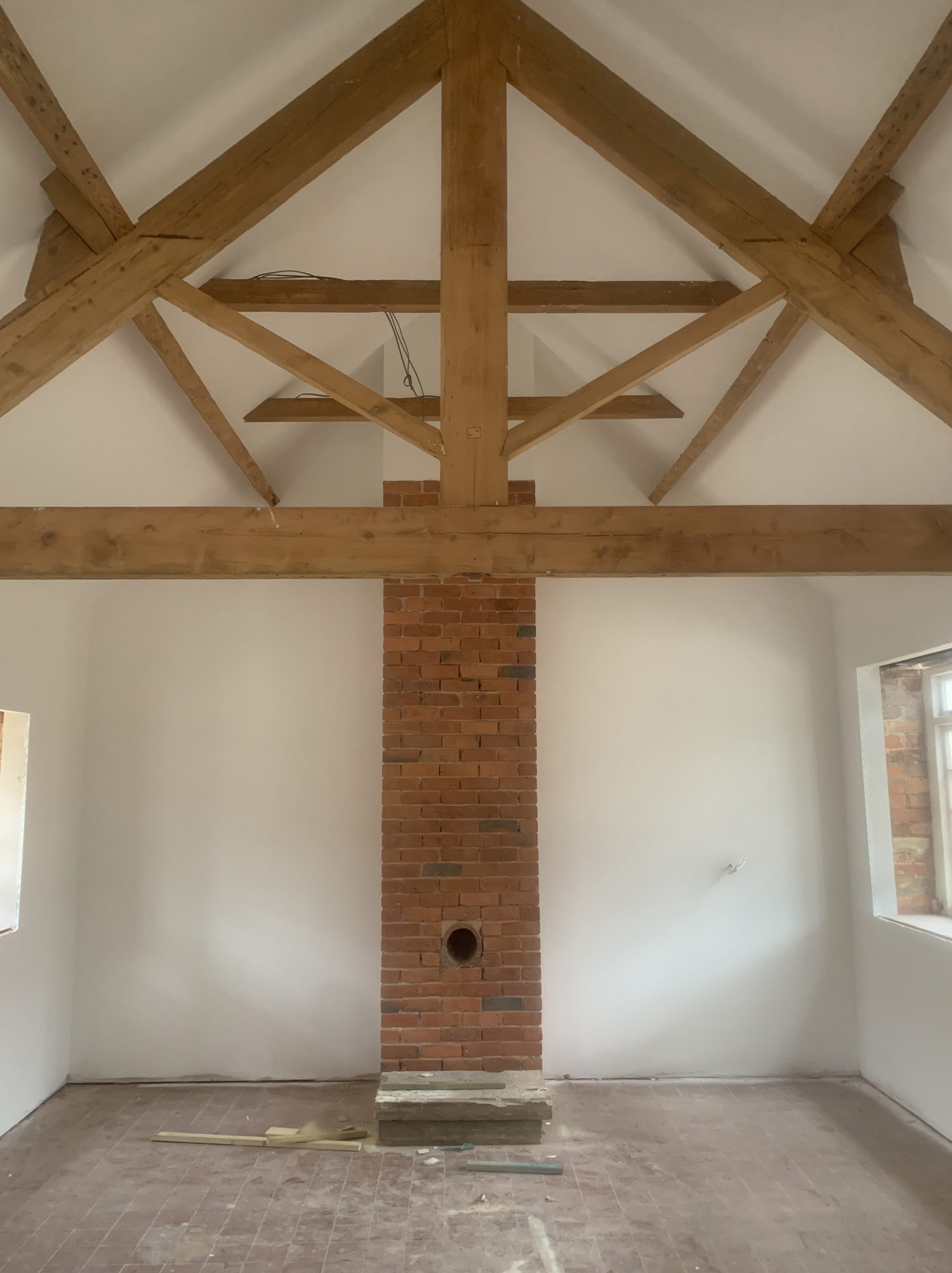 Living room with brick fire place and wooden rafters freshly plastered and painted white